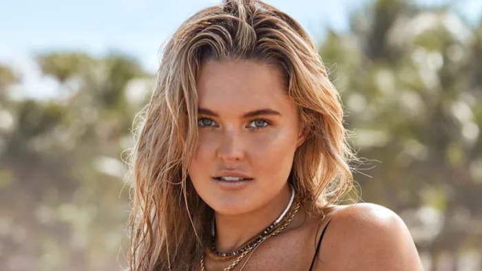 Georgina Burke poses in a string bikini and a stack of necklaces and looks at the camera.